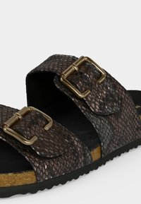 Sandale à enfiler avec deux brides texturées marron foncé dotées de boucles rectangulaires dorées et une semelle en liège avec une semelle extérieure noire.
