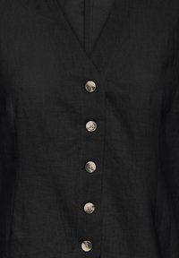 Gilet en lin noir avec un décolleté en V profond, comportant six boutons argentés à l'avant et une finition en tissu texturé.