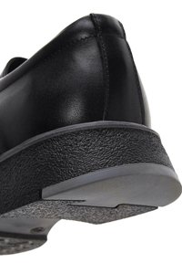 Zapato de cuero negro con una suela de goma texturizada. Diseño ovalado y detalle de costura visible en el talón.