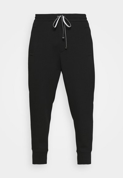 Zwarte joggingsbroek van zacht materiaal, met taps toelopende pijpen, een elastische tailleband en een witte koord met metallic uiteinden.