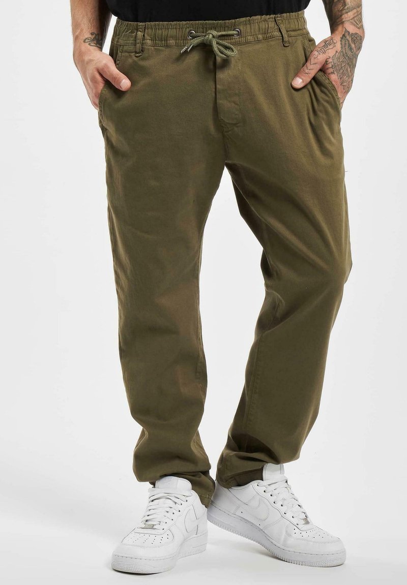 Pantaloni casual verde oliva con vita elasticizzata, chiusura con coulisse, tasche laterali e vestibilità comoda. Abbinati a sneakers bianche.