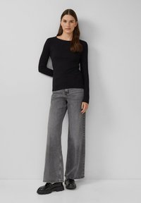 Zwarte longsleeve top gecombineerd met losse, grijze denim jeans. Stevige zwarte schoenen met een gestructureerde zool. Eenvoudig, minimalistisch ontwerp.