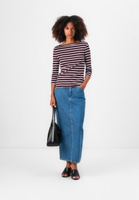 Gestreiftes, burgunderrotes und weißes Langarmoberteil, kombiniert mit einem langen Jeansrock in hellem Denim. Die Accessoires umfassen eine schwarze Handtasche und flache schwarze Sandalen.
