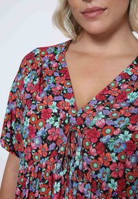Floral tunic with a V-neckline, featuring a black background and vibrant red, blue, and green flowers. Light, soft fabric with a tie detail.