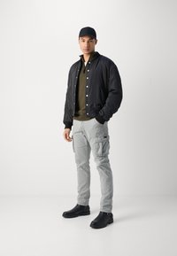 Black bomber jacket, olive zip-up, light gray cargo pants, and black boots. Simple design, contrasting colors, functional pockets.