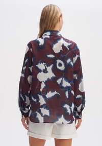 Langärmlige, burgunderfarbene Bluse mit floralem Muster in Blau und Weiß; leichtes Material mit lockerer Passform und knöpfbaren Manschetten.
