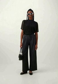 Black pleated top with short sleeves, paired with wide-leg dark gray trousers. Accessories include white sunglasses and a small black handbag.