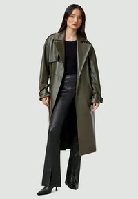 Woman wearing a dark green long leather trench coat over a black top and black wide-leg leather pants with heeled boots.