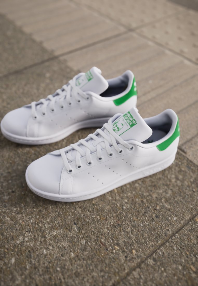Baskets en cuir blanc avec des accents verts sur le talon et la languette, présentant un design à lacets et des détails perforés sur les côtés.