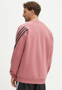 Felpa rosa con accenti a righe nere sulle spalle, realizzata in tessuto morbido, con polsini a costine e un design dalla vestibilità comoda.