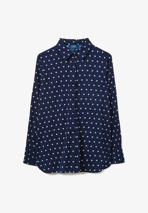 Chemise bleu marine à manches longues avec boutons, ornée de pois blancs et d'un col pointu, posée à plat sur un fond blanc.