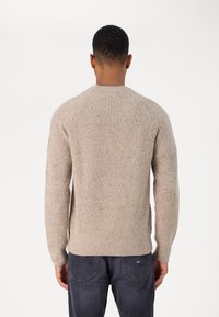 Beige knitted sweater with raglan sleeves, ribbed cuffs and hem, featuring a textured pattern. Worn with dark gray jeans.
