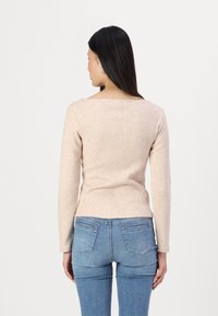 Helle beige Bluse mit langen Ärmeln, quadratischem Ausschnitt, taillierter Passform und weichem Material, kombiniert mit blauen Skinny-Jeans.