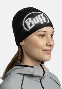 Black beanie with a textured finish featuring a large white "Buff" logo. It fits snugly and is paired with a gray jacket with an orange accent.