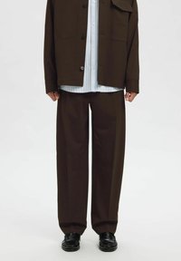 Ruda, per dydelį dydį siūta švarkas su sagomis, dėvimas ant šviesiai mėlynos dryžuotos marškinių. Plačiomis kojų rudos kelnės ir juodi batai užbaigia aprangą.