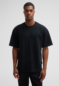 Zwarte t-shirt met korte mouwen, gemaakt van katoen, met een ronde hals en een losse pasvorm. Gladde textuur met minimale details.