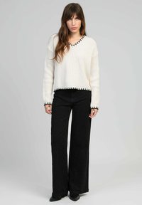 Pull en tricot blanc avec des finitions noires, col en V et manches longues, associé à un pantalon noir à jambes larges avec des détails subtils pailletés.