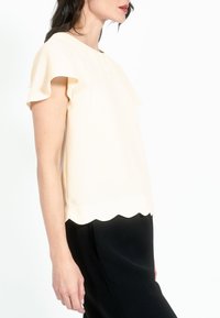 Helebeež blouse lühikeste volangkäistega ja lainelise äärega, kombineeritud mustade pükstega. Sujuv tekstuur, lihtne disain, mustreid pole.