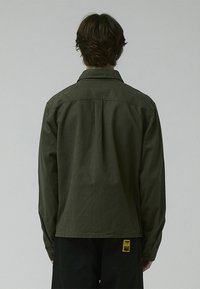 Olive green long-sleeve shirt made of cotton, featuring a classic collar and buttoned cuffs, with a straight hem and minimal seams.