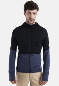 Hoodedá bunda s černými a námořnickými barevnými bloky, strukturovaná látka na vrchu, hladké rukávy, zip vpředu a otvory pro palce pro prodloužení rukávů.