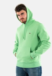Felpa verde menta con tasca a canguro, cappuccio regolabile con cordino e un piccolo logo sul petto. Tessuto morbido in misto cotone.