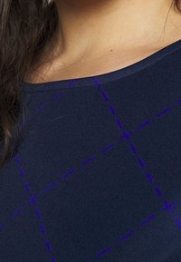Top blu navy con una texture morbida, caratterizzato da un motivo a griglia viola in contrasto e dettagli di cucitura lungo il collo.