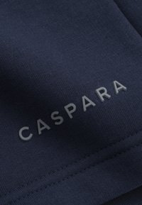 Marineblått stoff med en myk tekstur. Har ordet "CASPARA" i lys grått, plassert fremtredende på materialet.