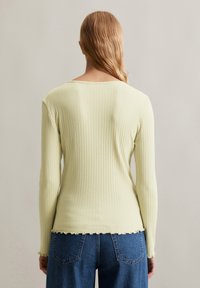 Lichtgele geribbelde lange mouw top met een ronde hals en een gekartelde zoom, gecombineerd met blauwe denim high-waisted jeans.