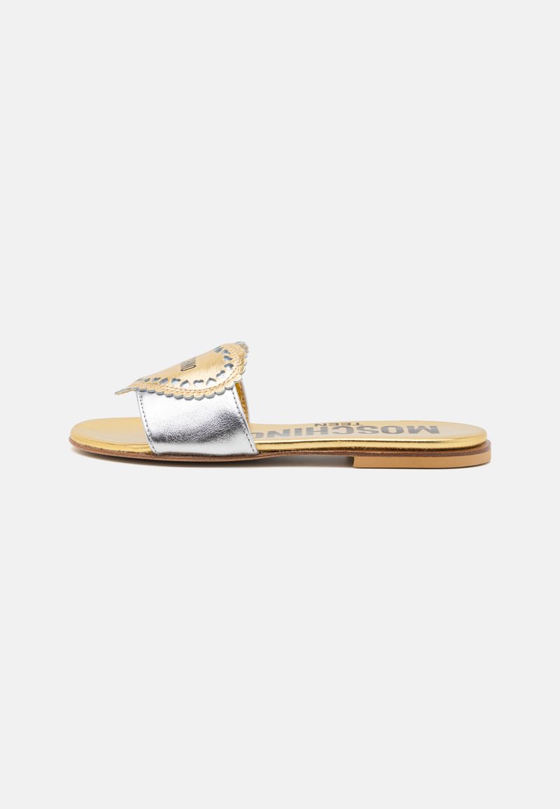Sandalia de slide metálica plateada con una tira con forma de concha, plantilla color tan y suela plana. Presenta un acabado texturizado y el logotipo de la marca en la plantilla.