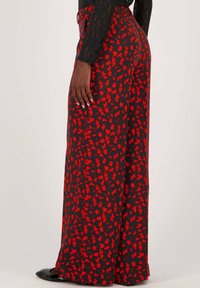 Wijde broek gemaakt van lichtgewicht stof, met een zwarte achtergrond en een rood bloemenpatroon. Elastische tailleband en zijslits.