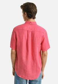 Kurzärmliges, pinkes Leinenhemd mit button-down Kragen. Verfügt über eine Rückennaht und einen abgerundeten Saum. Der Stoff hat eine strukturierte Oberfläche.