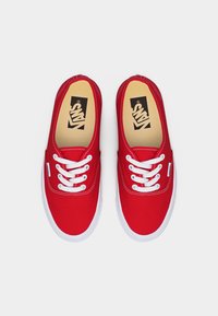 Ζευγάρι κόκκινων αθλητικών παπουτσιών Vans με λευκά κορδόνια και λευκές λαστιχένιες σόλες, σε άποψη από πάνω σε απλό φόντο.