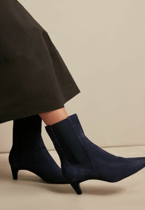 Stivaletti blu navy in suede con pannelli laterali elastici e punta affusolata, caratterizzati da un tacco sottile e una texture liscia.
