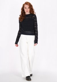 Granatowy sweter dziany z ażurowym wzorem, długimi rękawami i ściągaczem, w połączeniu z białymi spodniami o szerokich nogawkach i czarnymi butami.