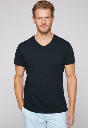 Camiseta negra de cuello en V con mangas cortas, que presenta un pequeño bolsillo en el pecho. Tejido suave con una textura lisa y un ajuste relajado.