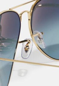 Ochelari de soare aviator din metal aurit cu lentile degradé de culoare albastră, având pad-uri nazale transparente și o bară subțire de sprijin care leagă lentilele.