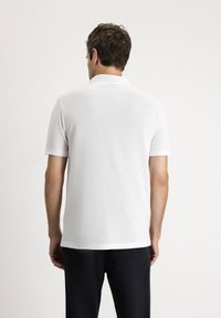 Biała koszulka polo wykonana z teksturowanej tkaniny, z płaskim kołnierzykiem i krótkimi rękawami. Prosty design bez widocznych logo ani wzorów.