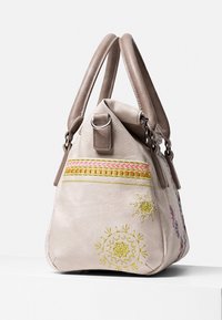 Beżowa skórzana torebka z podwójnymi uchwytami, haftowanymi kwiatowymi wzorami w odcieniach żółci i różu oraz trójkątnym kształtem z dekoracyjnym paskiem.