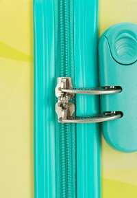 Fermeture à glissière turquoise avec un tirant et un verrou en métal, complétée par un boîtier en plastique lisse. L'arrière-plan présente un jaune vif avec des motifs subtils.