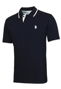 Polo de color azul marino hecho de algodón, con un cuello blanco y un logo bordado en el lado izquierdo del pecho. Mangas cortas con acentos contrastantes.
