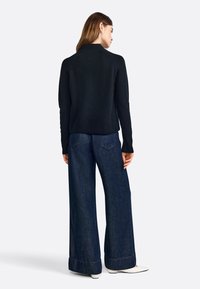 Black, textured sweater with a high neck, paired with wide-leg dark denim jeans featuring a folded cuff. Minimalist design with a clean silhouette.
