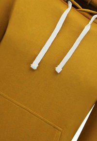 Mosterdgele hoodie gemaakt van zachte stof, met een voorzak, witte trekkoorden en ribgebreide boorden en zoom.
