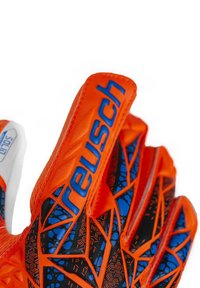 Orange goalkeeper gloves feature a textured grip with blue accents and a geometric pattern. Brand name "Reusch" prominently displayed on the thumb.