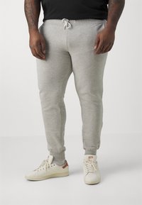 Grå joggebukser med elastisk midje og snøring, med smale ben og ribbestrikkede mansjetter. Kombinert med hvite sneakers.