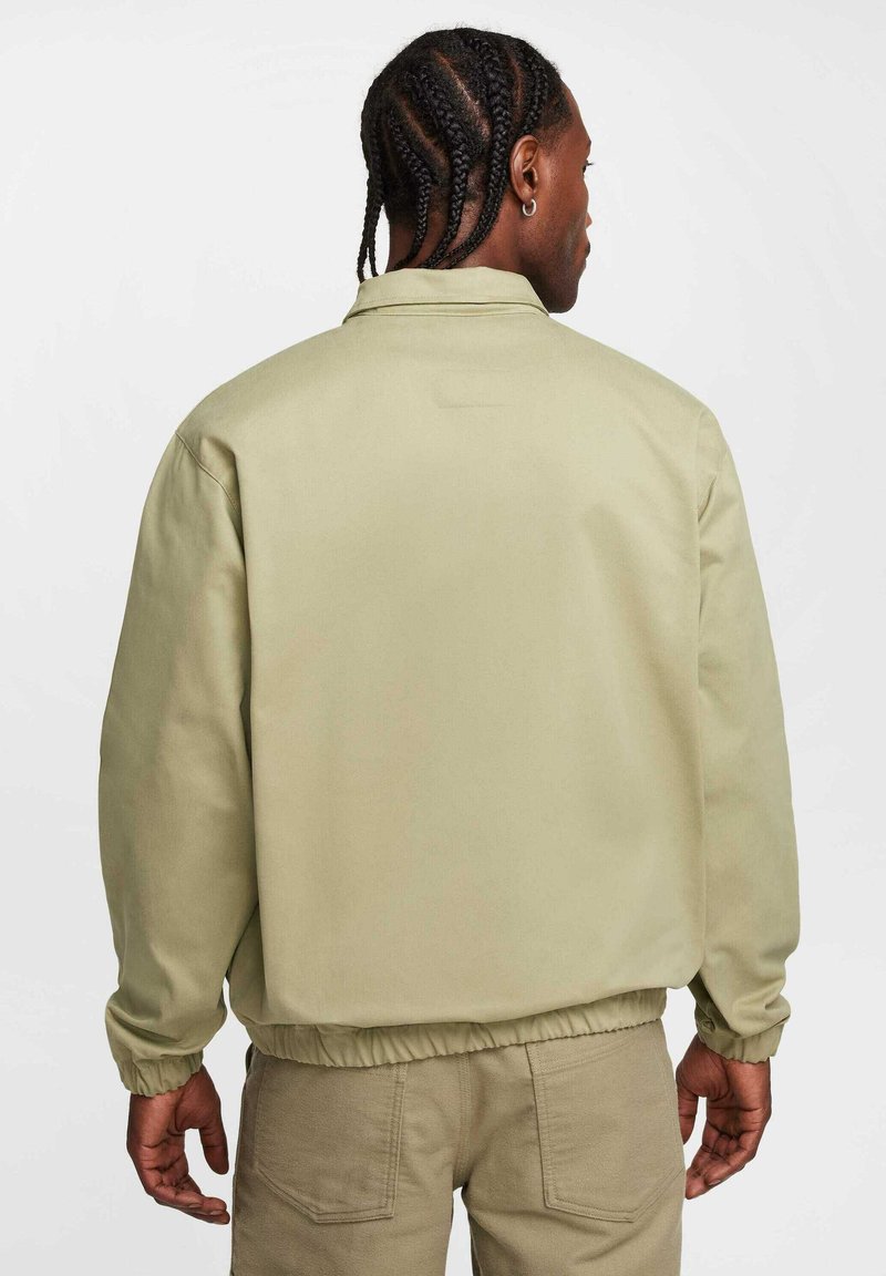 Chaqueta bomber de color verde claro con puños y cinturilla elásticos, que presenta una textura suave y un diseño minimalista. Sin marcas visibles.