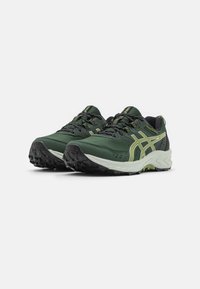 Zapatillas deportivas verdes con un empeine texturizado, acentos amarillos contrastantes, cordones negros y una suela negra resistente para proporcionar tracción.