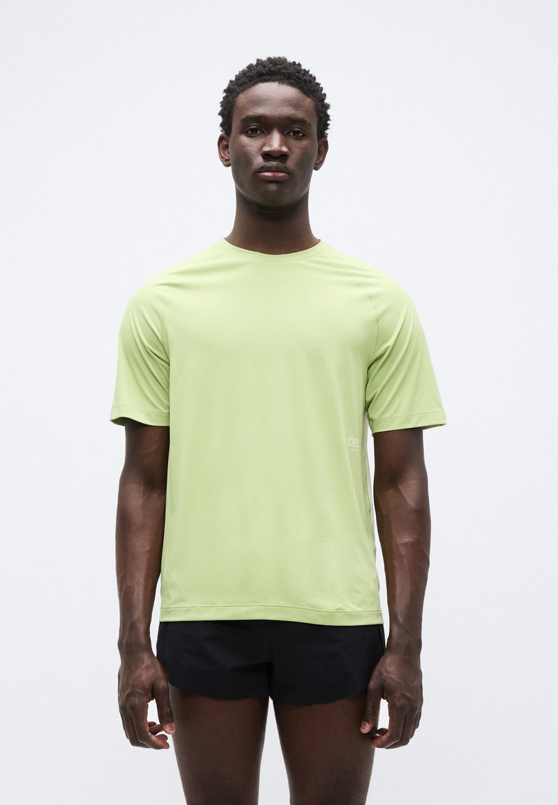 Αθλητική κοντομάνικη μπλούζα ανοιχτού πράσινου με στρογγυλή λαιμόκοψη και λεία υφή, σε συνδυασμό με μαύρο σορτς. Διαθέτει μικρό λογότυπο στο πλάι.