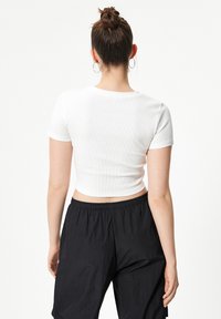 Camiseta blanca recortada de manga corta, con textura acanalada y cuello redondo, combinada con pantalones negros de corte holgado.