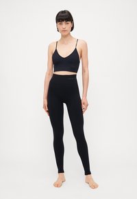 Svart sportsbh med tynne stropper og V-hals, kombinert med høyt midje svart leggings. Glatt tekstur, tettsittende design.