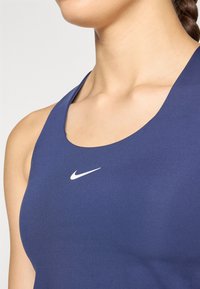 Tamnoplavi atletski top bez rukava s okruglim izrezom, izrađen od glatke, rastezljive tkanine, s bijelim Nike logom na grudima.